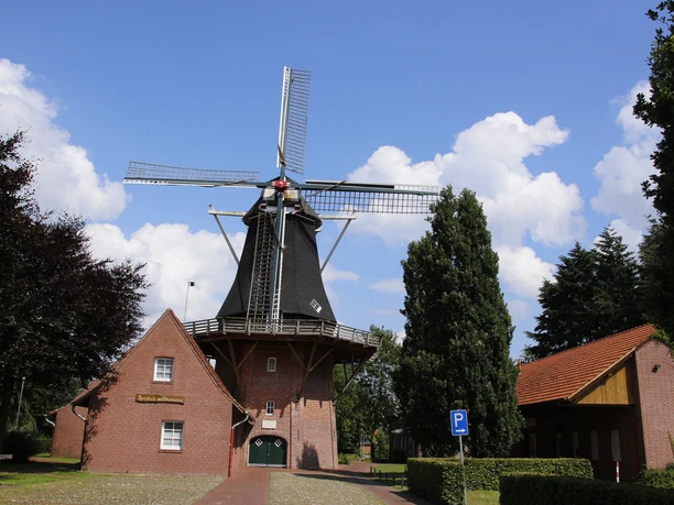 Kreutzmanns Mühle Historische Windmühle mit rotem Backsteinsockel und Holzflügeln vor blauem Himmel in Werlte.