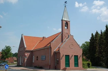 Lathen Backsteinkirche in Lathen mit spitzem Turm, grünem Portal und rotem Ziegeldach unter blauem Himmel