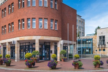 Lingen Wirtschaft + Tourismus GmbH Moderne Touristeninformation in rotem Klinkerbau mit Glasfront und bunten Blumenkübeln davor