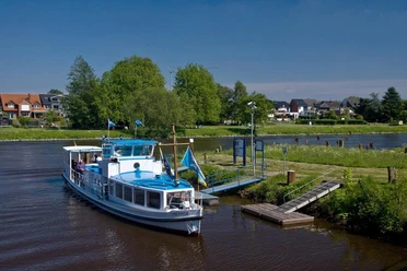 Maritime Meile Haren (Ems) Personenschiff mit blau-weißem Deck legt an einem Anleger an der Ems in Haren vor grüner Uferkulisse an.