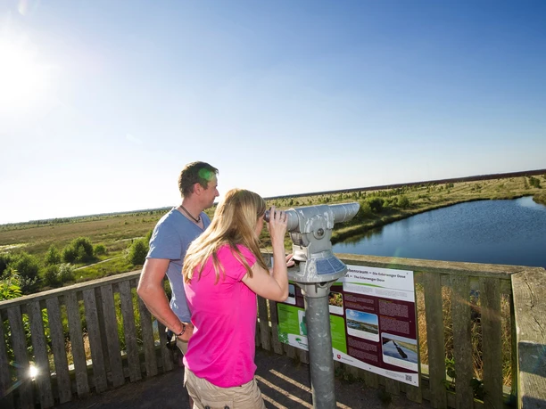 MoorInfoPfad Esterwegen Zwei Personen blicken von einer hölzernen Aussichtsplattform auf Moorlandschaft mit Wasserfläche.