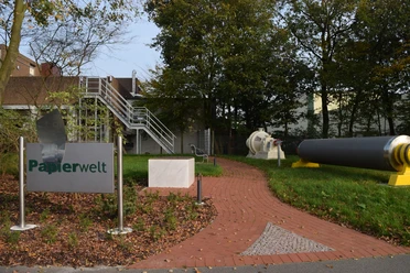 Papierwelt Dörpen Eingangsbereich der Papierwelt Dörpen mit Infotafel, rotem Weg und großen Papiermaschinen-Teilen.
