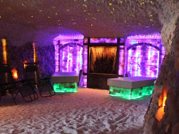 Salzgrotte Hasetal Raum aus Salzsteinen mit Sandboden, Liegestühlen und farbiger Beleuchtung zur Entspannung.