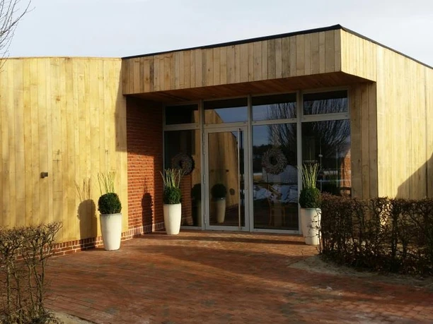 Eingang zur Salzgrotte Moderner Eingang mit Glasfront und Holzverkleidung, flankiert von Pflanzkübeln auf rotem Klinkerweg.