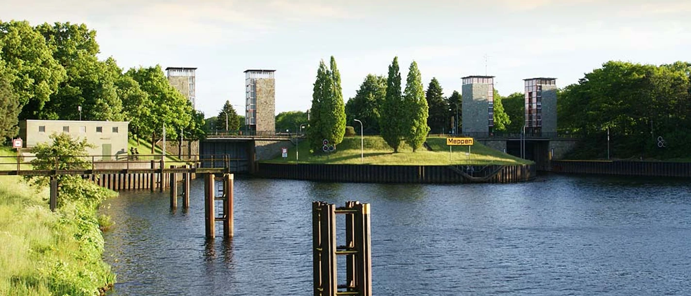 Schleuse Meppen Wasserweg mit Schleusenanlage in grüner Umgebung, moderne Türme und Bäume im Hintergrund.