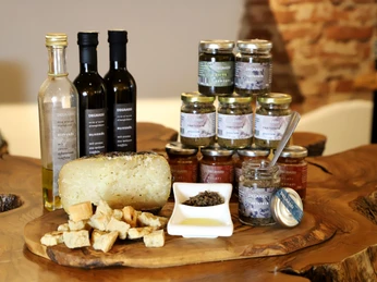 Eine Auswahl an Olivenölen, Pasten und Brotstücken auf einem Holztisch, im Hintergrund sind Ziegelwände sichtbar.