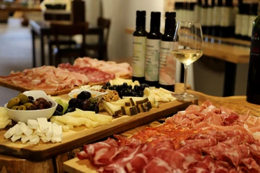 Italienische Antipasti-Platten mit Aufschnitt, Käse und Oliven, begleitet von Weißwein auf Holztafeln.