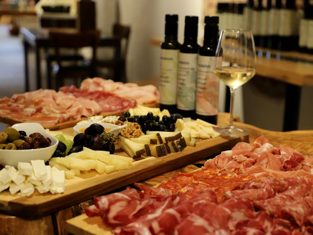 IMG_9201.JPG Italienische Antipasti-Platten mit Aufschnitt, Käse und Oliven, begleitet von Weißwein auf Holztafeln.