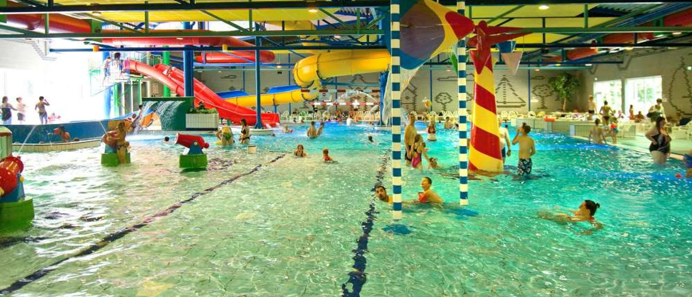 Spaßbad Topas Buntes Hallenbad mit Rutschen, Wasserspielen und fröhlichen Badegästen in lebendiger Atmosphäre