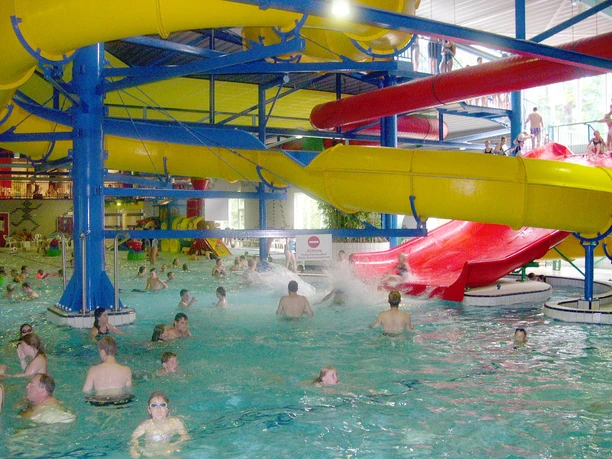 Spaßbad Topas Buntes Hallenbad mit gelben und roten Wasserrutschen, vielen Badegästen und spritzendem Wasser.