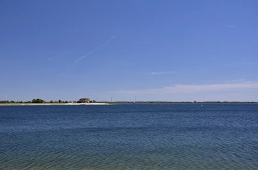 Speichersee Geeste Blauer See mit klarem Wasser unter wolkenlosem Himmel, Ufer mit Strandhaus und Windrädern in der Ferne.