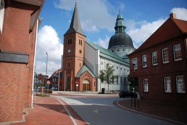 St.-Martinus-Kirche in Haren (Ems) Backsteinkirche mit hohem Turm und großer Kuppel zwischen roten Ziegelhäusern unter blauem Himmel