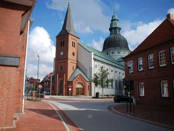 St.-Martinus-Kirche in Haren (Ems) Backsteinkirche mit hohem Turm und großer Kuppel zwischen roten Ziegelhäusern unter blauem Himmel