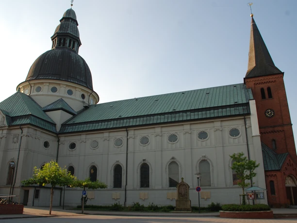 St.-Martinus-Kirche in Haren (Ems) Backstein-Kirchturm mit Uhr und großes Kirchenschiff mit grüner Kuppel unter blauem Himmel.