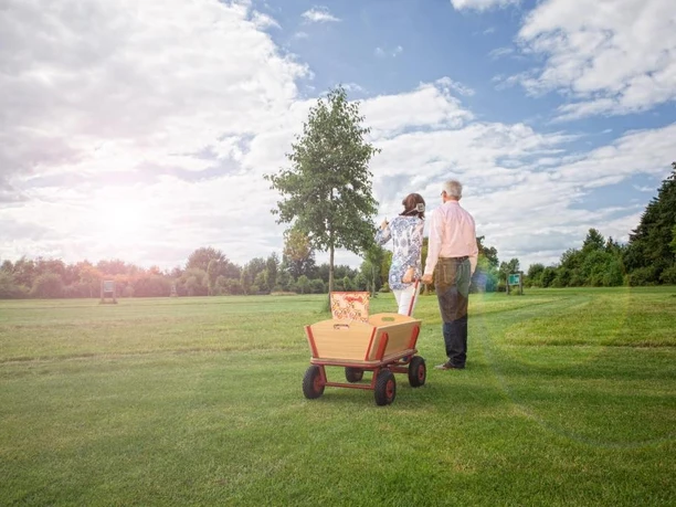 SwinGolf Mehringer Heide Zwei Personen gehen über eine weitläufige Wiese mit SwinGolf-Ausrüstung unter leicht bewölktem Himmel.