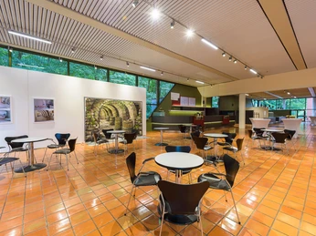 Theater an der Wilhelmshöhe Heller, großzügiger Foyerbereich mit Tischen, Stühlen und Ausstellungswänden im Theater an der Wilhelmshöhe.