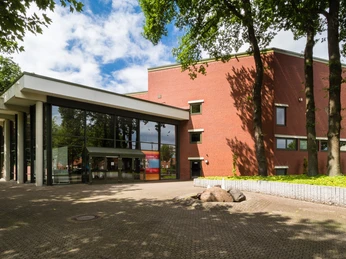 Theater an der Wilhelmshöhe Backsteinbau mit großer Glasfront und Säulengang, umgeben von Bäumen, Eingang mit Vordach.