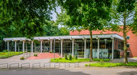Theater an der Wilhelmshöhe Moderne Theaterfassade mit Glasfront, umgeben von Bäumen und barrierefreiem Zugang.