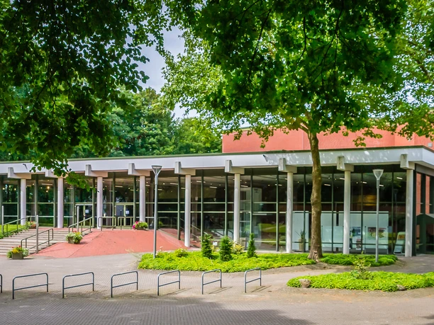Theater an der Wilhelmshöhe Moderne Theaterfassade mit Glasfront, umgeben von Bäumen und barrierefreiem Zugang.
