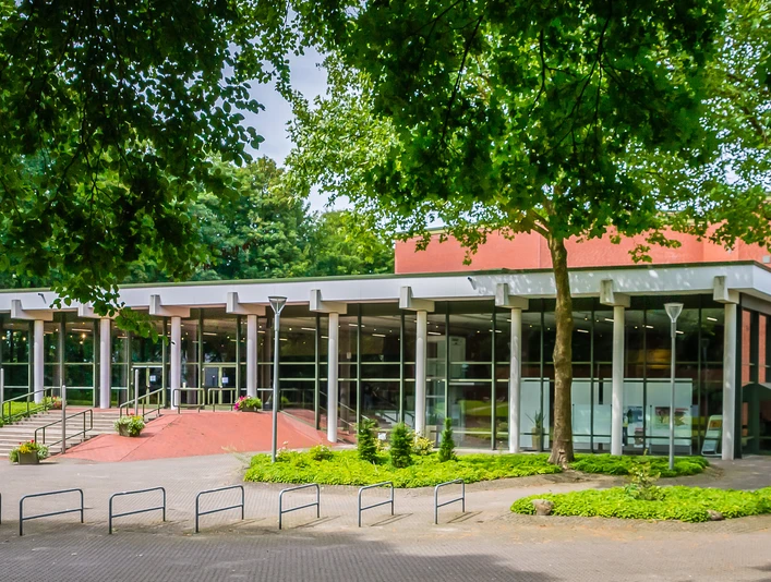 Theater an der Wilhelmshöhe Moderne Theaterfassade mit Glasfront, umgeben von Bäumen und barrierefreiem Zugang.