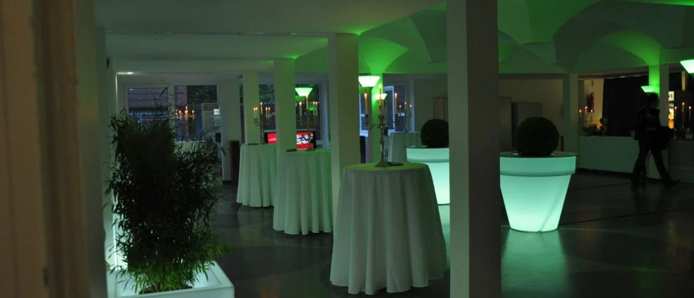 Theater im Windthorstgymnasium Meppen Beleuchteter Empfangsraum im Theater Meppen mit hohen Stehtischen und grüner Lichtgestaltung.