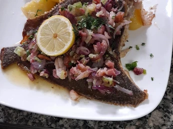 Scholle Finkenwerder Art Gebackene Scholle mit Speck, Zwiebeln, Knoblauch, Zitrone und Kartoffeln auf einem weißen Teller.