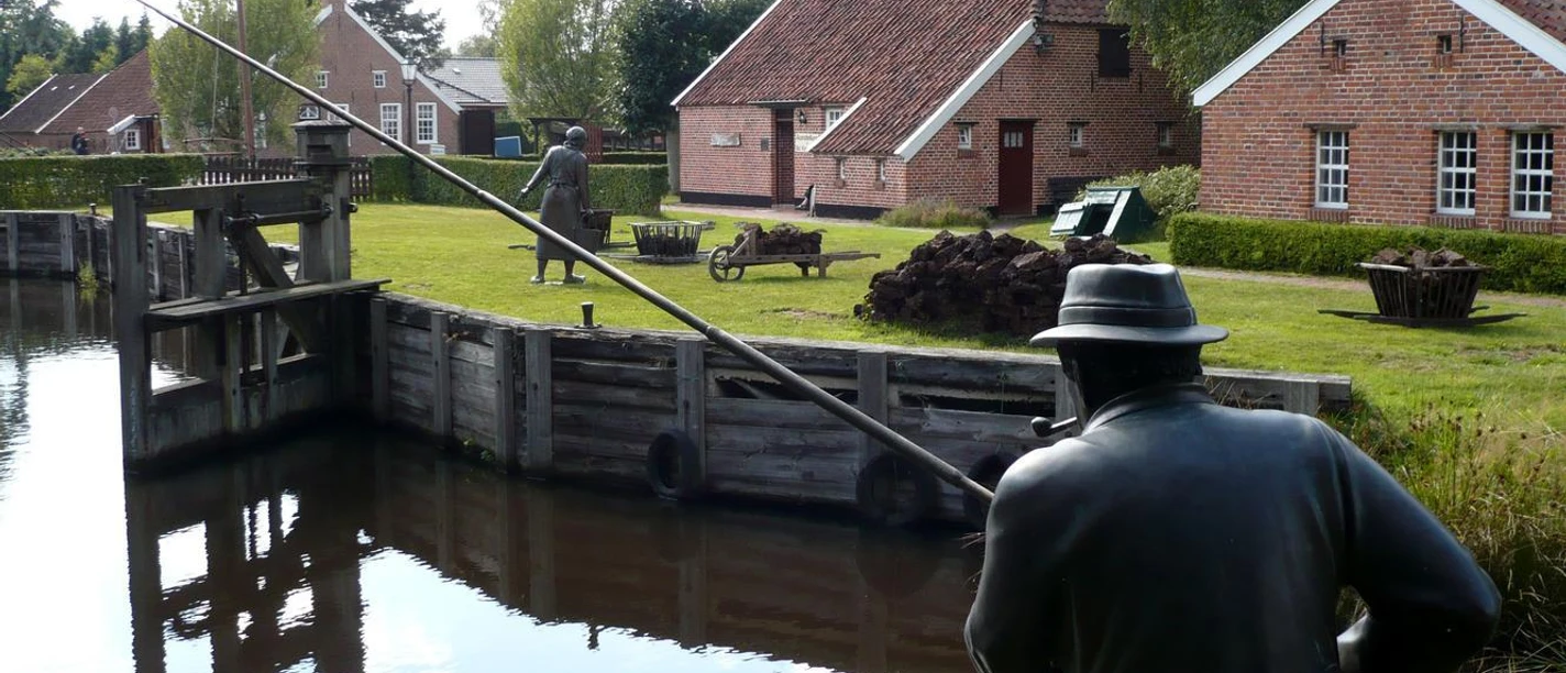 Von-Velen-Anlage Historische Moorlandschaft mit Backsteinhäusern, Holzschleuse und Bronzefiguren am Wasser in Papenburg