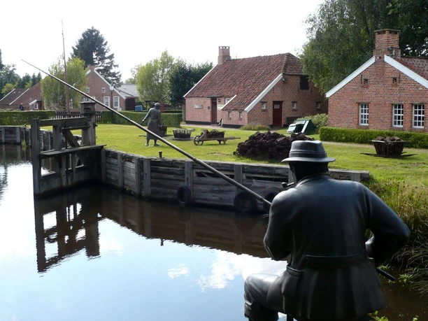 Von-Velen-Anlage Historische Moorlandschaft mit Backsteinhäusern, Holzschleuse und Bronzefiguren am Wasser in Papenburg