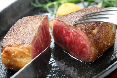 wagyubudefleisch.jpg Angebratenes Wagyu-Steak mit rosa Kern auf dunklem Teller, angeschnitten und saftig glänzend.