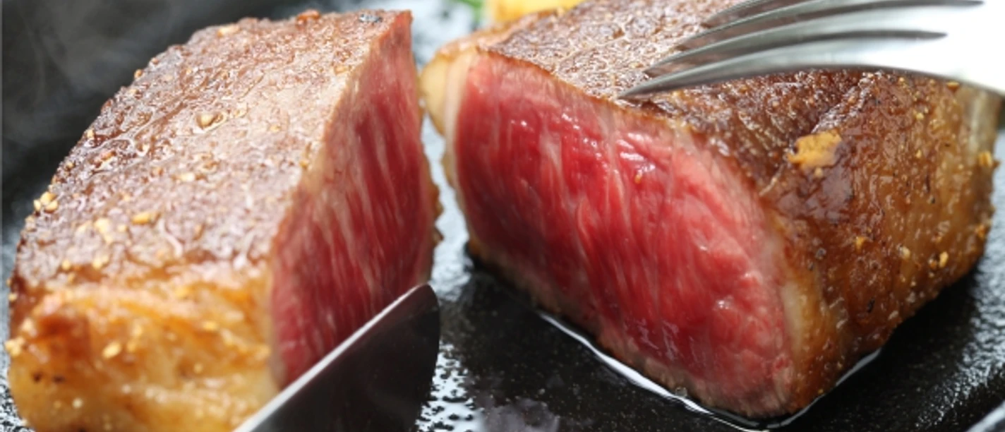 wagyubudefleisch.jpg Angebratenes Wagyu-Steak mit rosa Kern auf dunklem Teller, angeschnitten und saftig glänzend.