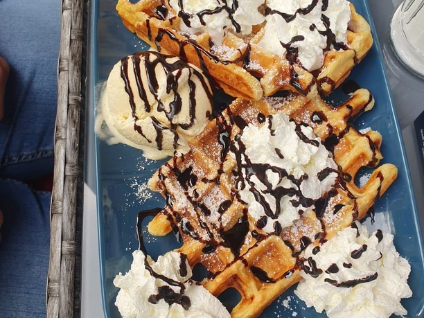 Waffeln mit Vanilleeis, Schlagsahne und Schokosauce auf blauer Platte sorgen für Genussvielfalt.