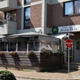 Jever Deele Außenansicht Gasthaus mit rotem Backstein, markantes Jever Deele-Schild über der Eingangstür, Sonnenschirm.