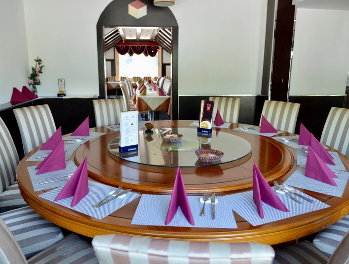 Ein großer runder Holztisch ist elegant gedeckt mit violetten Servietten und Besteck.