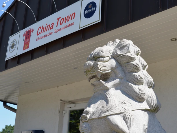 Steinlöwe bewacht den Eingang eines asiatischen Restaurants mit chinesischen Spezialitäten in urbaner Umgebung.