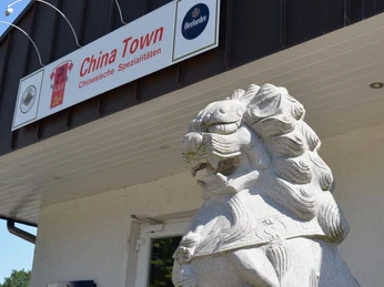 Außenansicht China Town Steinlöwe bewacht den Eingang eines asiatischen Restaurants mit chinesischen Spezialitäten in urbaner Umgebung.