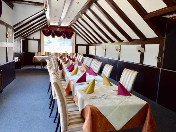 Raum für Festgesellschaften Festsaal mit langer Tafel, gedeckt mit farbigen Servietten unter Holzbalken, ideal für Veranstaltungen.