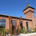 Eisenhütte Backsteinindustriegebäude mit Turm und großen Fenstern vor klarem Himmel; moderne Kunstinstallation vorne.
