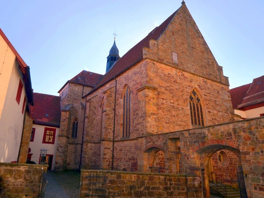 Historische, steinerne Kirche mit gotischen Fenstern und Satteldach bei Tageslicht.