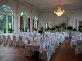 spiegelsaal-festlich-dekoriert Ein prächtig dekorierter, historischer Spiegelsaal mit eleganten Tafeln und blütenreichen Blumenarrangements.