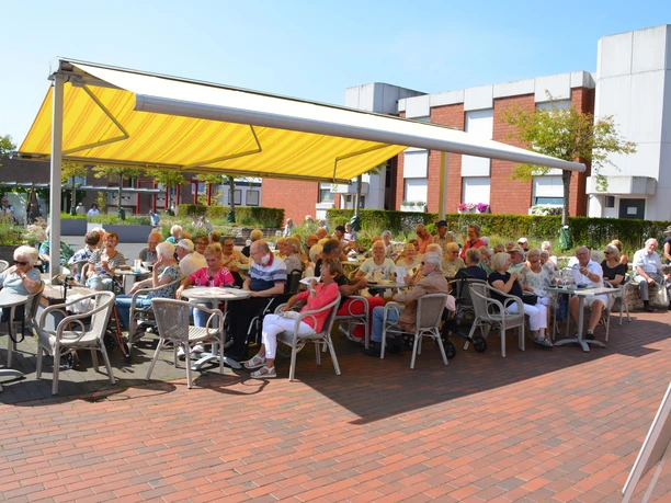 Schattiges Plätzchen Seniorengruppe genießt sonnigen Tag unter gelbem Sonnendach, umgeben von Backsteingebäuden.