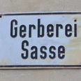 Die alte Gerberei Sasse Historisches Metallschild mit der Aufschrift "Gerberei Sasse" auf beigem Hintergrund.