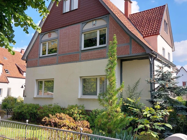 Ein charmantes Haus mit einem Garten und grünen Pflanzen. Der Himmel ist klar und blau, was eine freundliche Atmosphäre schafft.