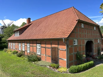 Historisches Fachwerkhaus mit roten Ziegeln und Sprossenfenstern, umgeben von grüner Natur.