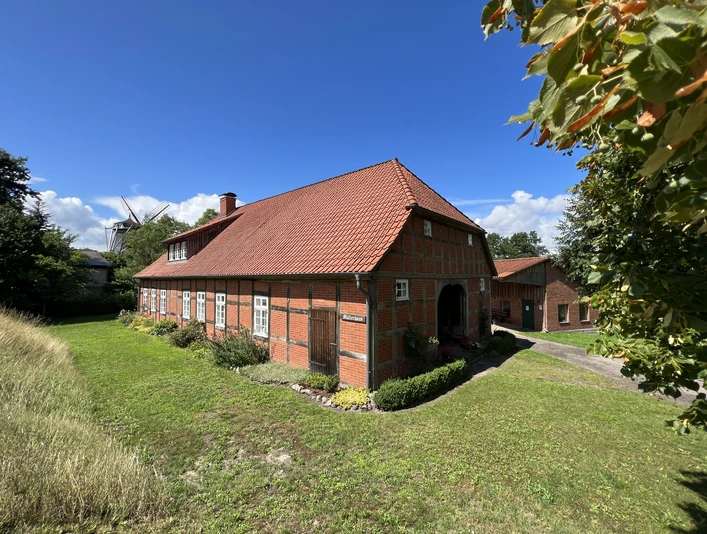 Müllerhaus Historisches Backsteinhaus mit rotem Satteldach, umgeben von grüner Wiese, unter blauem Himmel.