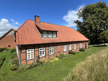 Altes Müllerhaus mit rotem Ziegeldach, Fachwerkdetails und umgeben von grüner Natur.