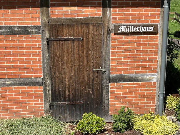 Rotes Ziegelgebäude mit Holzrahmen, einer braunen Holztür, daneben das Schild "Müllerhaus".
