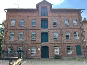 Backstein-Wassermühle mit grünen Türen und Fenstern, in einem flachen, gepflasterten Vorhof.