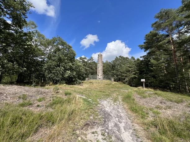 Lindhoopdenkmal Langer Gedenkstein umgeben von Wiese und Bäumen unter strahlend blauem Himmel mit weißen Wolken.