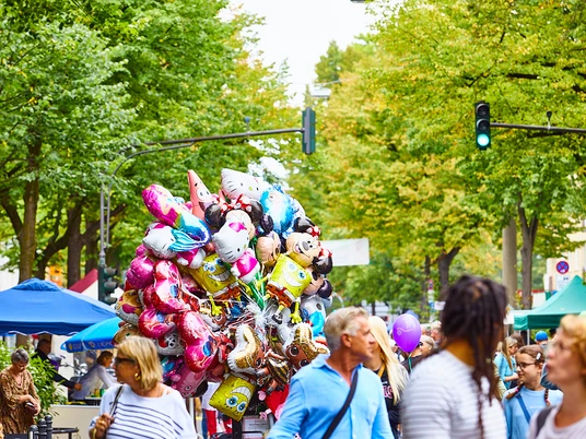 Lindenthal summer festival Lebendiges Sommerfest auf der Dürener Straße mit bunten Ballons vor grünen Bäumen und fröhlichen Besucher*innen.Lively summer festival on Dürener Straße with colorful balloons in front of green trees and happy visitors.