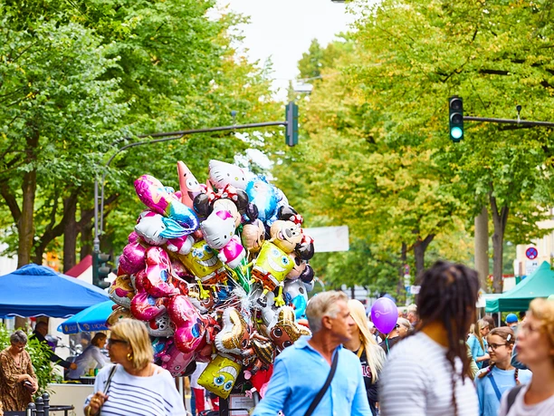 Lindenthaler Sommerfest Lebendiges Sommerfest auf der Dürener Straße mit bunten Ballons vor grünen Bäumen und fröhlichen Besucher*innen.